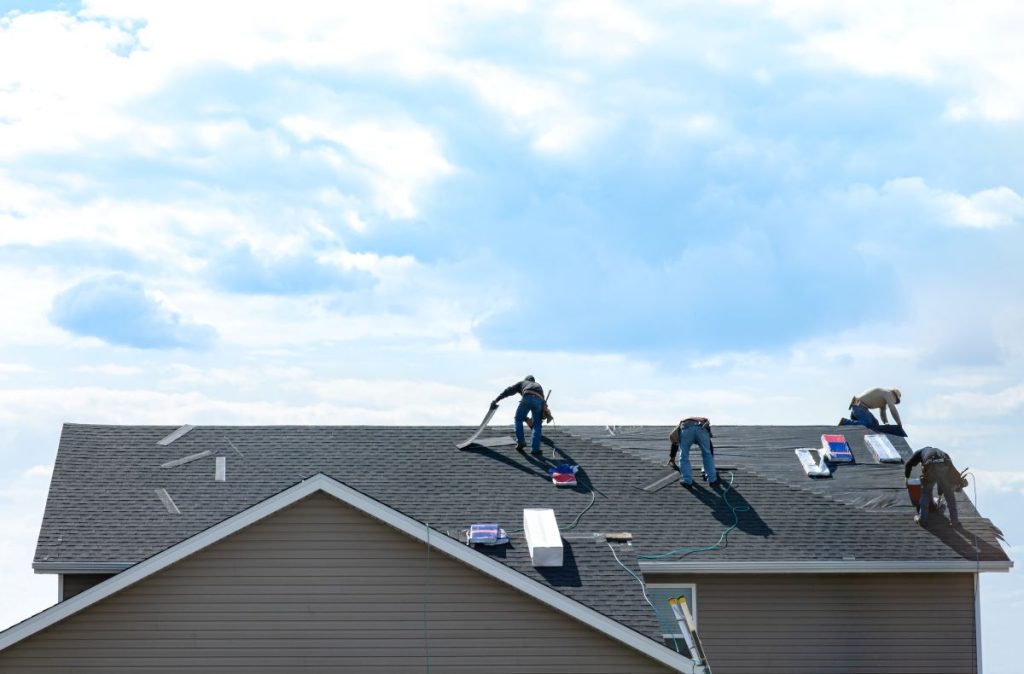 4 construction workers fixing roof against clouds blue sky, install shingles at the top of the house, North Oaks, Minnesota